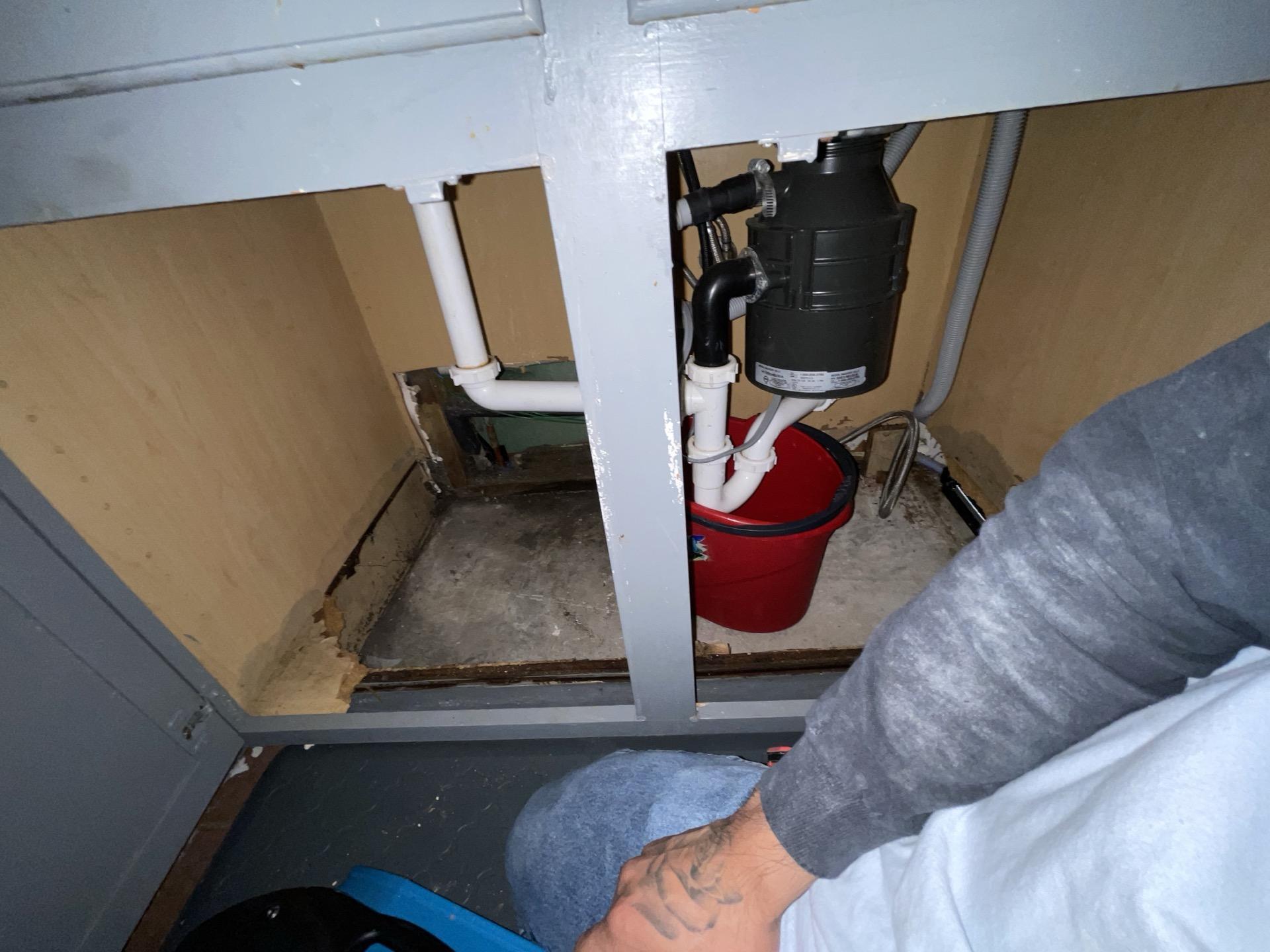 Water leak visible under kitchen cabinets with pooling moisture on cabinet floor
