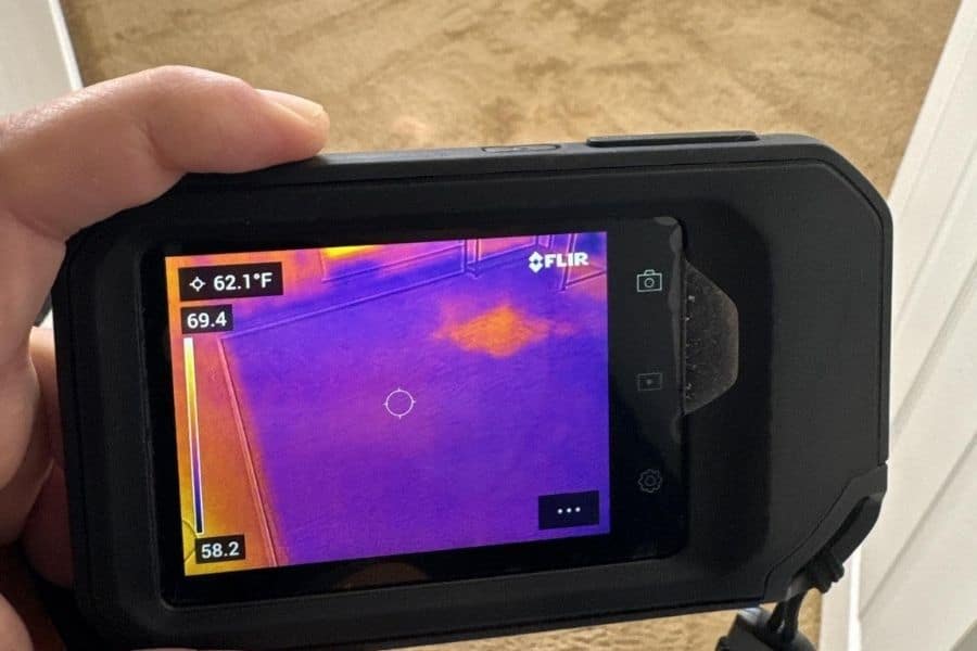 Restoration technician using a thermal imaging camera to detect hidden moisture behind walls in a Plano TX home