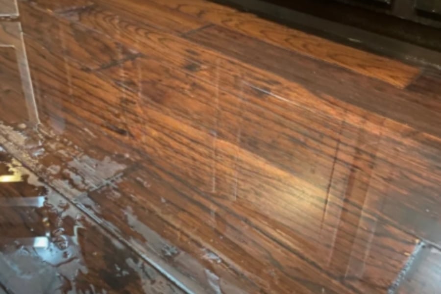 Standing water pooling on a wooden kitchen floor in a Plano home after an appliance leak