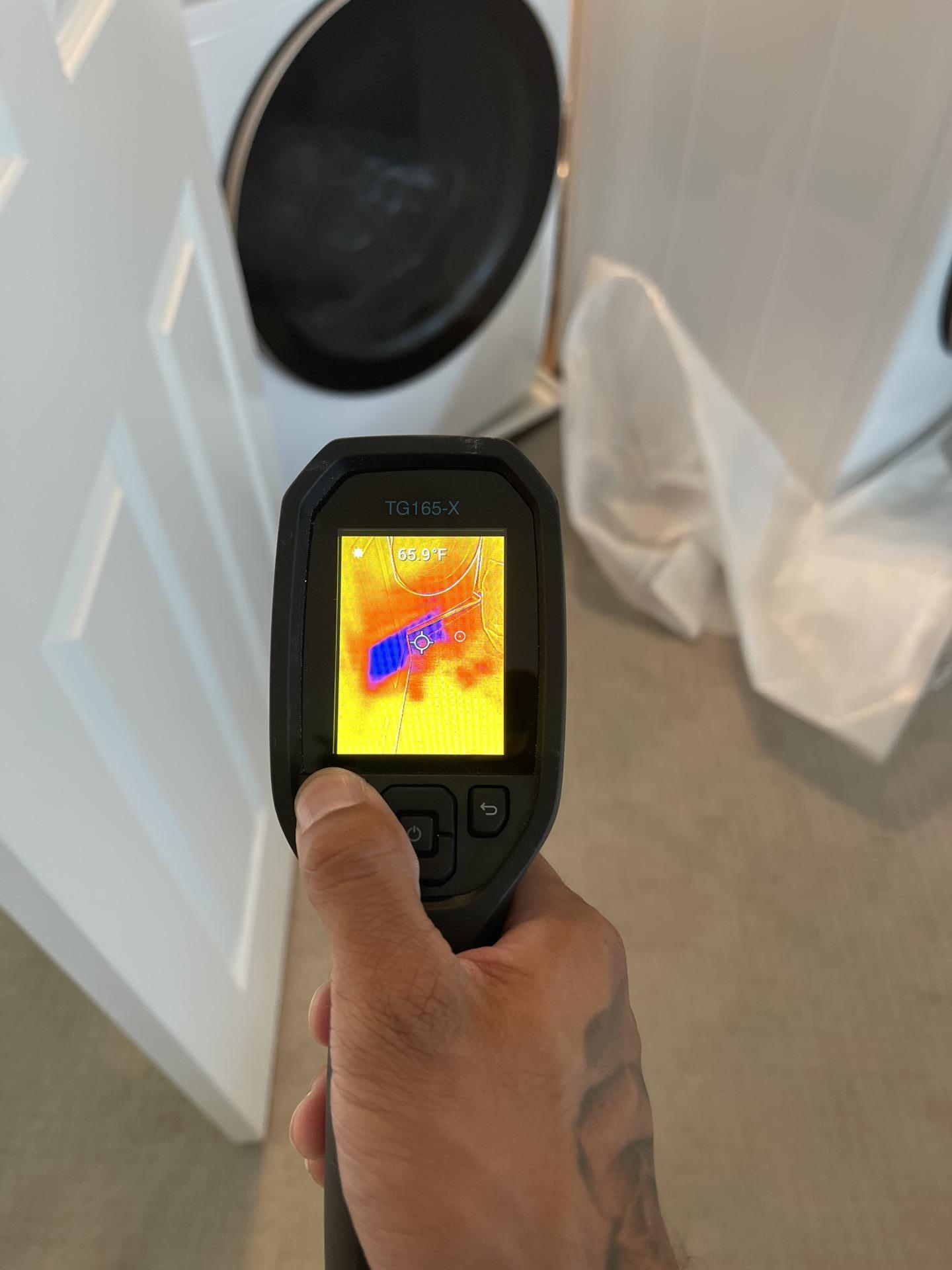 Technician using a thermal imaging camera to find hidden moisture after a washing machine leak